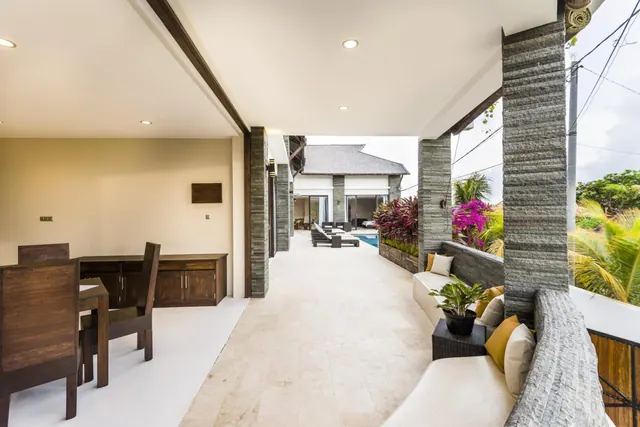 A covered terrace with cushioned sofa seating and a dining table, with a small pool and sun loungers visible beyond.