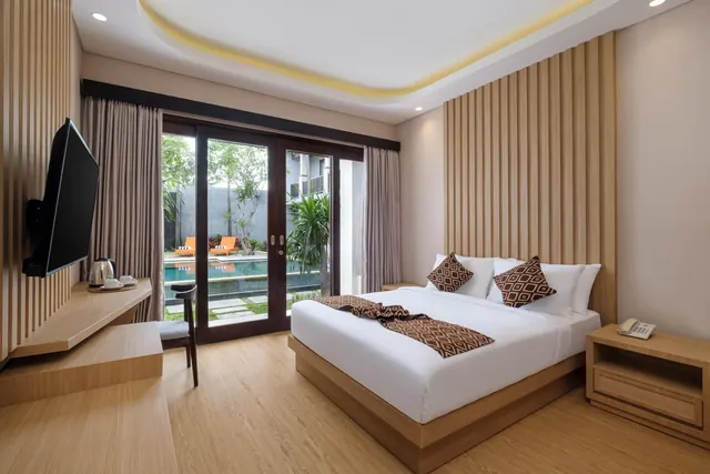 A bedroom with a king bed, a wall-mounted television and glass doors opening onto a pool and garden.