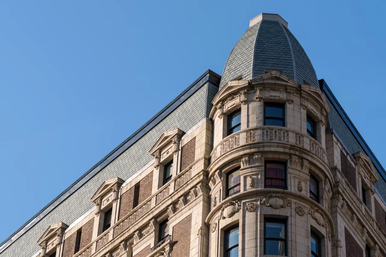 Looking up at the stone and brick corner tower of a historic building with a domed slate roof under a clear blue sky.