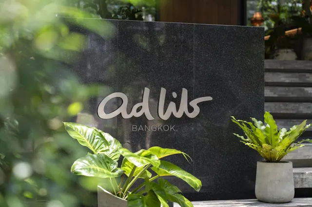 The ad lib Bangkok logo is mounted on a dark granite wall beside potted plants and stone steps at the entrance.