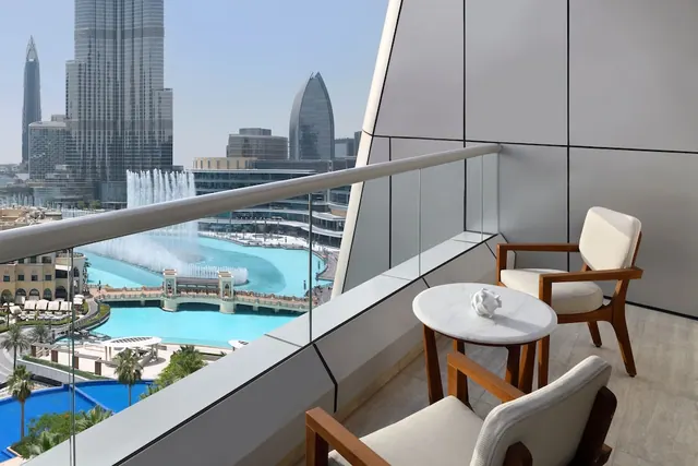 A private balcony with two cushioned armchairs and a round marble side table overlooks the Burj Khalifa, the Dubai Fountain lake and a pool below.