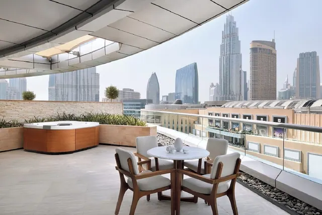 A rooftop terrace with a hot tub, a round table and four chairs, overlooking high-rise towers under a hazy sky.