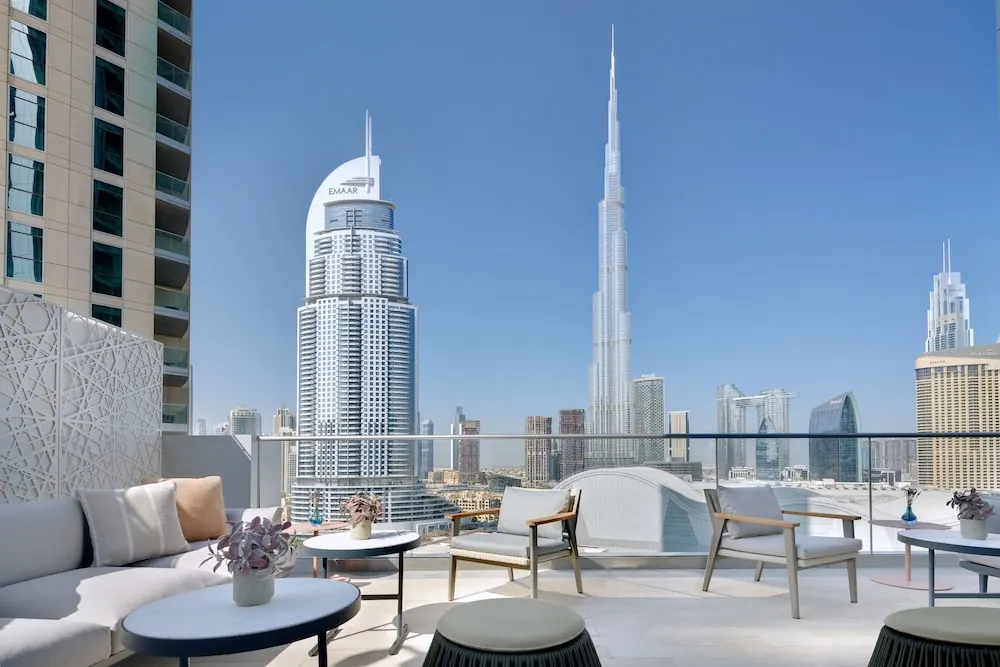 A furnished terrace with a sofa, armchairs and side tables overlooks the Burj Khalifa and surrounding skyscrapers under a clear blue sky.
