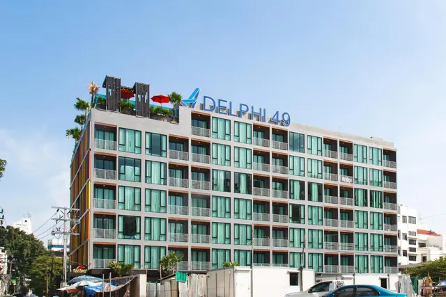 The exterior of the Delphi 49 hotel building, with its name on the facade and umbrellas on the rooftop, under a clear blue sky.