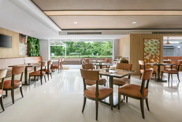A bright dining room with tan leather chairs and tables on a glossy white floor, with large windows looking out onto trees.
