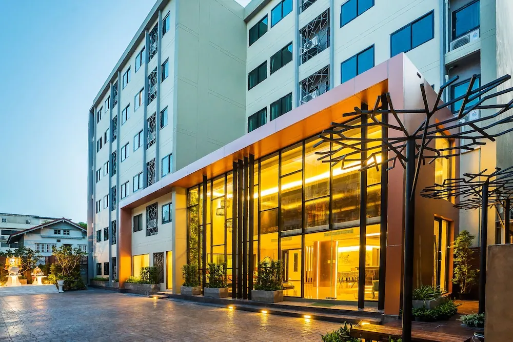 The hotel's multi-storey facade and illuminated glass entrance are shown at dusk, with a black metal tree sculpture beside the courtyard.