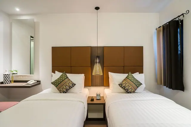 Two single beds with white linen and patterned cushions sit against a padded brown headboard, with a pendant lamp hanging above and a phone on a wall-mounted shelf to the left.