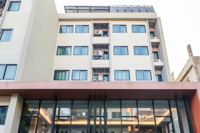 Low-angle view of a multi-storey hotel building with a glass-fronted ground floor and a red-brown canopy, with air conditioning units visible on some windows.