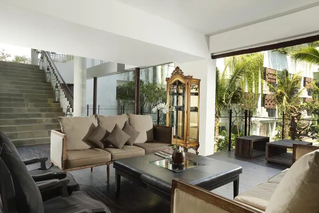 A covered lounge area with a sofa, leather coffee table, gold display cabinet and stone steps, opening onto a garden with palm trees.