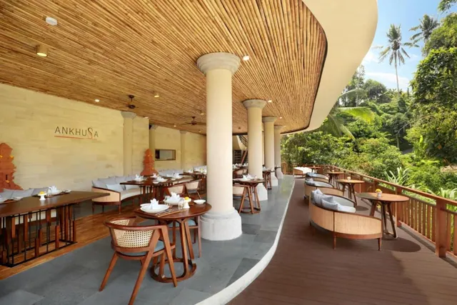 An open-air restaurant terrace with a bamboo ceiling, white columns, wooden tables and cane chairs, with tropical greenery visible beyond the railing.