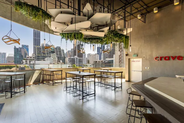 A dining area with high tables and stools, hanging planters and a city skyline visible through the open side.
