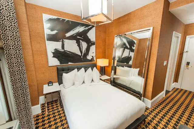 A bedroom with a king bed, tufted black headboard, large abstract painting, floor mirror and patterned carpet.