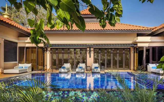 A private pool sits in front of a villa with a terracotta roof, white sun loungers with blue cushions, and glass doors onto the terrace.