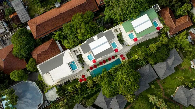 Aerial view of a hotel with a rectangular pool, red umbrellas, small plunge pools and terracotta-roofed buildings around it.