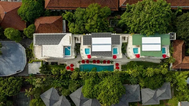 Aerial view of a resort with three villas, each with a small pool, and a larger central pool surrounded by red umbrellas.