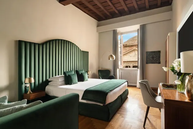 A bedroom with a king bed, green velvet headboard and armchair, and a window showing the dome of the Pantheon outside.