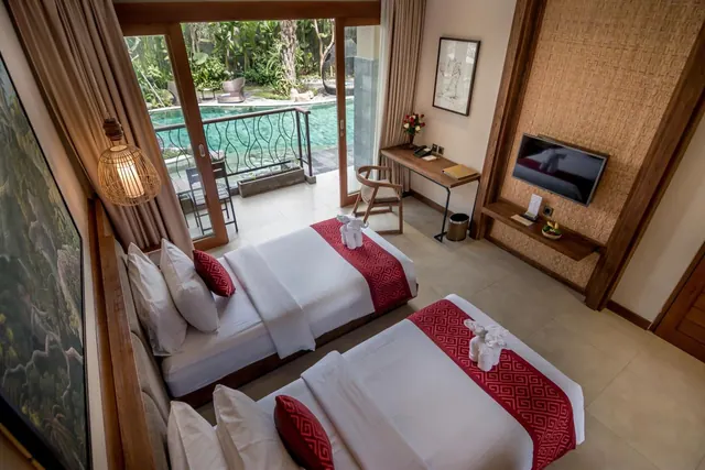 A twin-bedded room with red runners and towel animals on the beds, with glass doors opening onto a balcony overlooking a pool and garden.