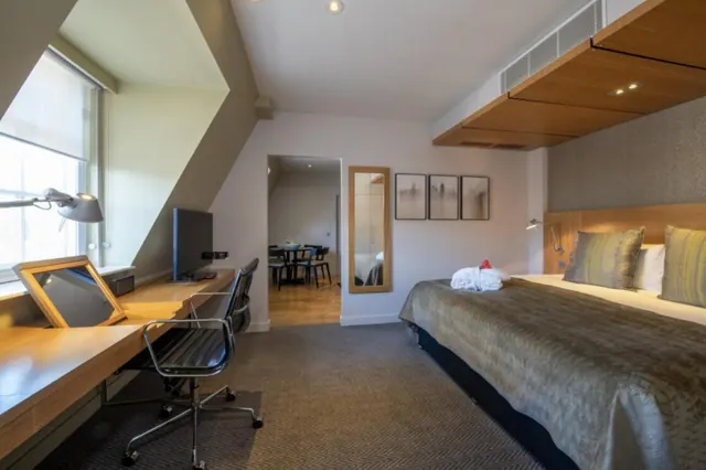 A hotel bedroom with a double bed, a desk with a chair and a television, and a doorway through to another room.