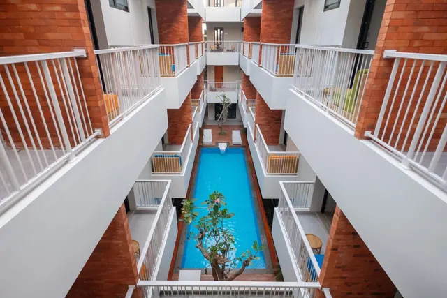 Elevated view down into a courtyard with a long swimming pool, a small tree, and white balconies on brick-faced walls.