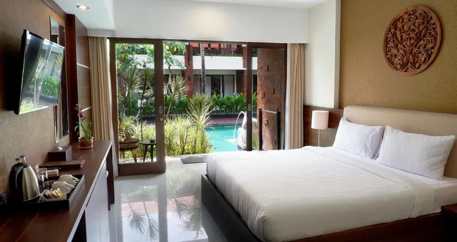 A bedroom with a king bed, wall-mounted television and tea tray, with glass doors opening onto a garden and swimming pool.