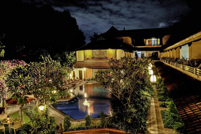 Night view of an illuminated courtyard pool with a fountain, sun loungers, lanterns and a traditional Balinese-style building.