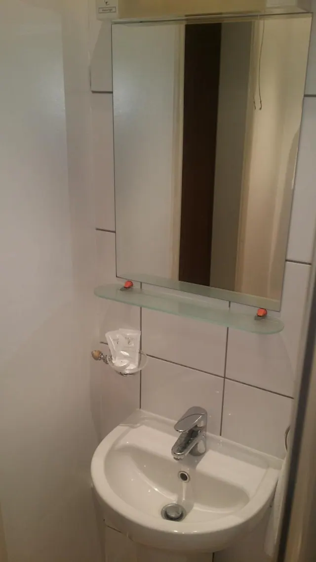 A small bathroom with a white wash basin, chrome mixer tap, wall mirror above a glass shelf, and white wall tiles.