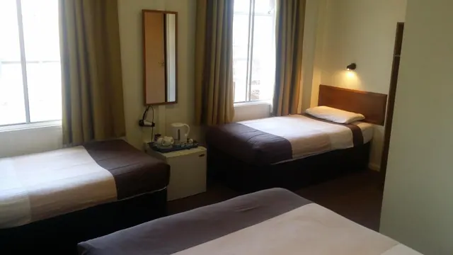 A hotel bedroom with single beds, a wall mirror, and a kettle and tray on a small white fridge between the beds.