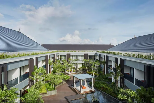 Elevated view of a hotel courtyard with two-storey wings, a timber walkway, planted beds, and a canopied daybed over a water feature.