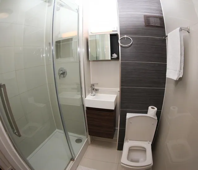 A bathroom with a glass-enclosed walk-in shower, a wall-mounted basin with a dark vanity unit, a wall-hung toilet and a white towel on a rail.