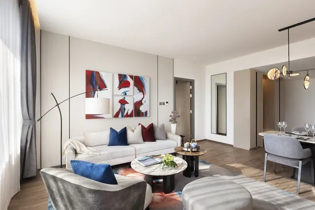 A living area with a light sofa, colourful cushions, round marble coffee tables and a red and white abstract artwork on the wall, with a dining table visible at right.