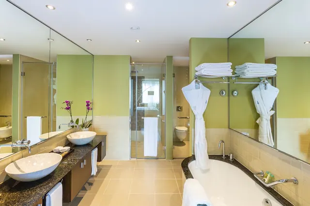 A bathroom with a double vanity of two vessel sinks, a freestanding bathtub, a glass-walled walk-in shower, and folded towels and bathrobes on wall racks.