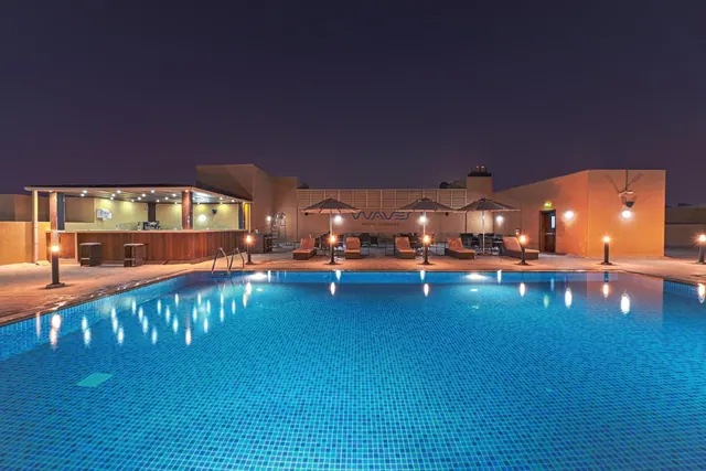 A large illuminated swimming pool at night with a bar counter, umbrellas and sun loungers on the surrounding deck.