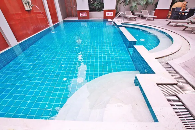 A tiled swimming pool with stone steps, a wall spout, depth markers showing 100 and 120 cm, and sun loungers on the deck.