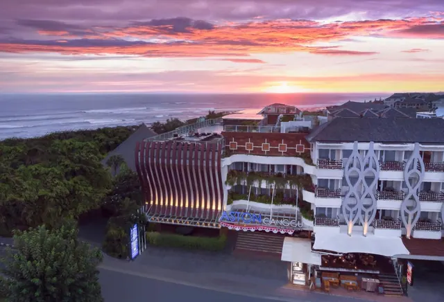 Aerial view of the Aston Canggu hotel building at sunset, with the ocean and colourful sky behind it.