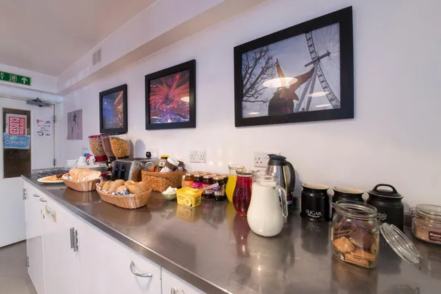 A breakfast counter with bread baskets, jams, juice, a milk jug, cereal dispensers and sugar jars, with framed photos of the London Eye and other scenes on the wall above.