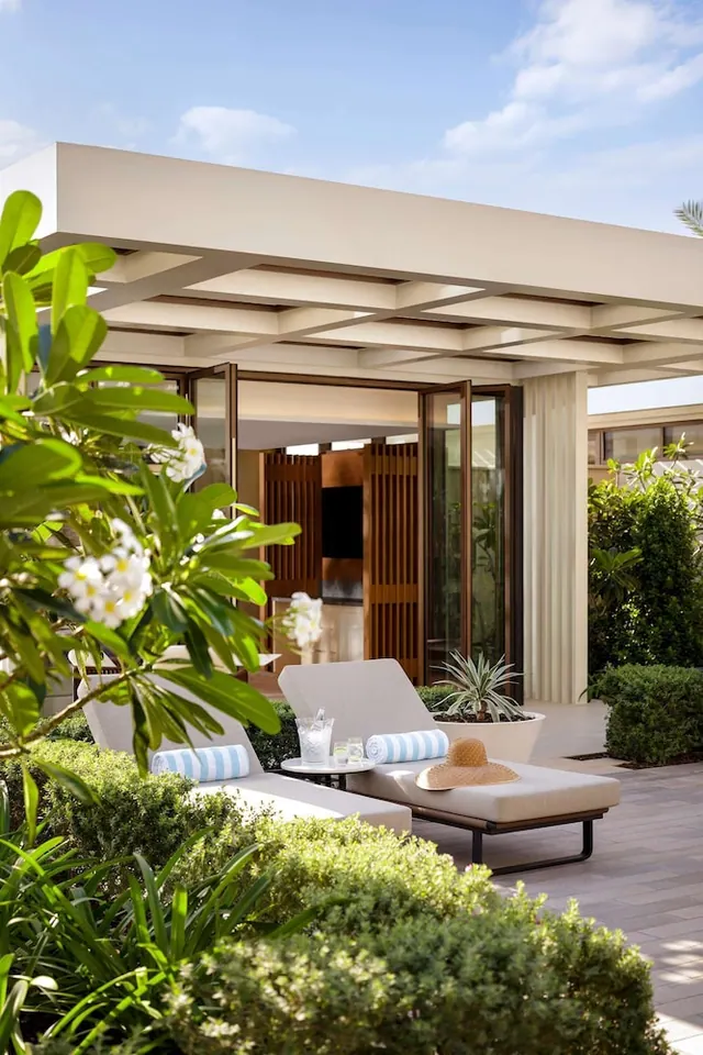 A covered terrace with two sun loungers, striped towels, a small side table with glasses, and potted plants beside glass doors.