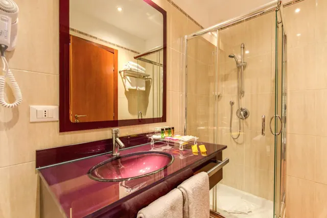 A bathroom with a magenta glass vanity and oval sink, a glass-enclosed walk-in shower, and towels hanging on a rail.
