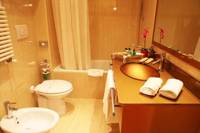 A bathroom with a bathtub behind a shower curtain, a toilet and bidet, and a round basin on a vanity with folded white towels.
