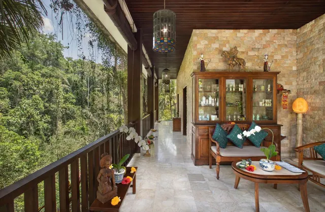 A covered terrace with wooden sofa and coffee table, a glass display cabinet and hanging lanterns, with dense green jungle visible beyond the railing.