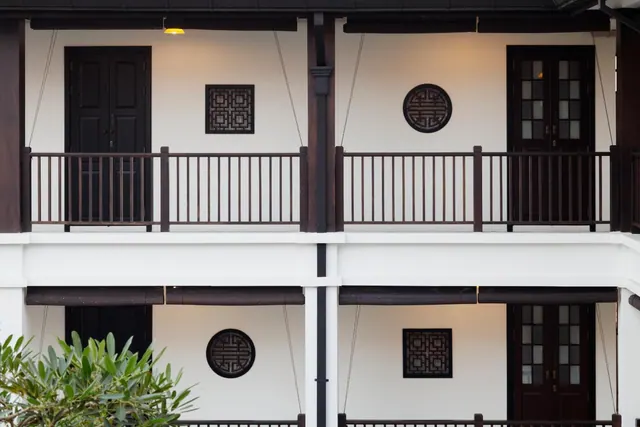 The exterior of a two-storey white building with dark wooden balconies, railings, decorative lattice panels and French doors.