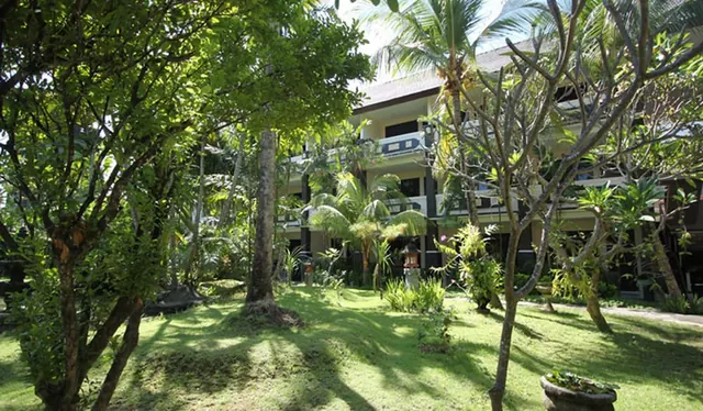 A grassy lawn with tall trees and palms in front of a multi-storey hotel building with balconies.