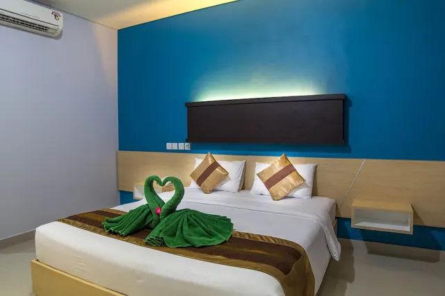 A bedroom with a double bed dressed with green towel swans, a blue accent wall, a wooden headboard and a wall-mounted air conditioner.