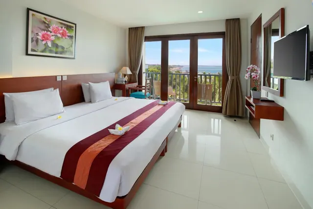A bedroom with a king bed, a wall-mounted television and French doors opening onto a balcony with a view of the sea.