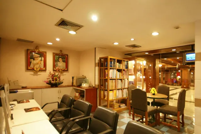 A lobby area with a reception counter, leather armchairs, a bookshelf, a round table with chairs, framed portraits on the wall and a wall-mounted television.