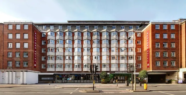 Street-level view of the front of the Bedford Hotel, a red brick building with cream bay windows, with traffic lights, a lamp post and planters on the pavement.