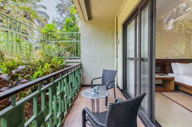 A furnished balcony overlooks dense tropical planting beside a room with a double bed.
