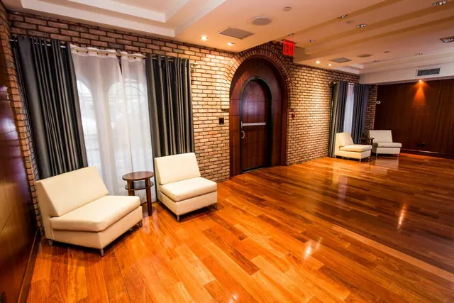 A seating area with cream armchairs and a small round side table, an arched wooden door set into a brick wall, and a polished wooden floor.