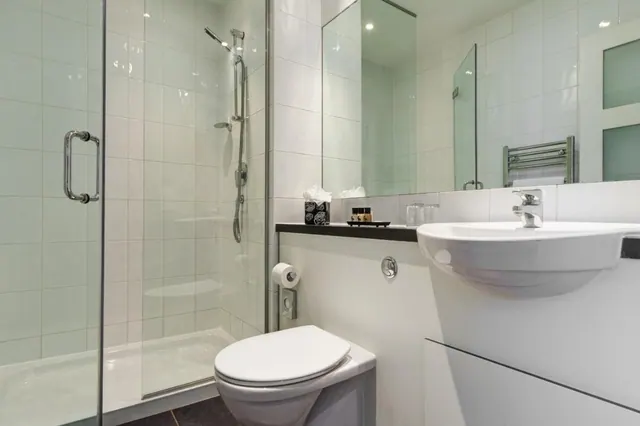 A bathroom with a walk-in glass shower, a wall-mounted toilet, and a wall-hung basin with a chrome tap beside a heated towel rail and mirror.