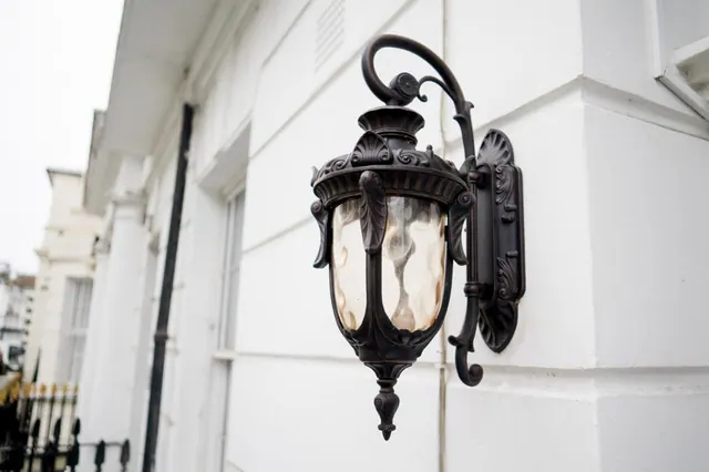 An ornate black wall lantern with textured glass panels is mounted on a white rendered building facade.
