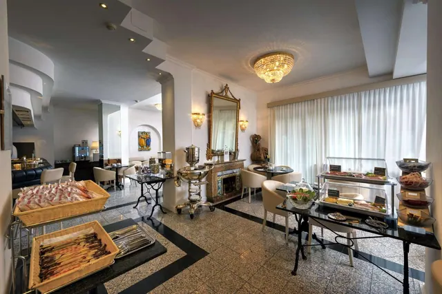 A breakfast room with food baskets and glass display cases on a buffet counter, small tables and chairs, a gilded mirror, a fireplace and a crystal chandelier.